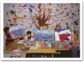 Photo of young students standing in front of our Tree of Life mural